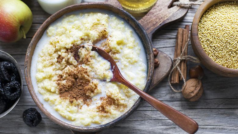 Wooden bowl of porridge with brown spoon on rustic table with grains and fruit
