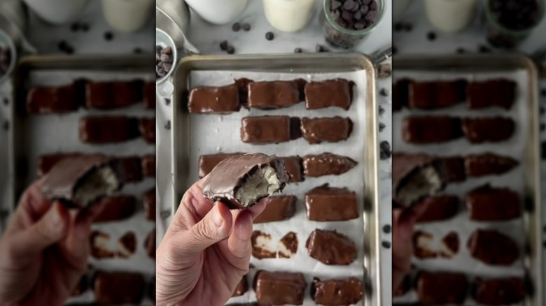 Hand holding piece of chocolate potato candy over tray of other candies
