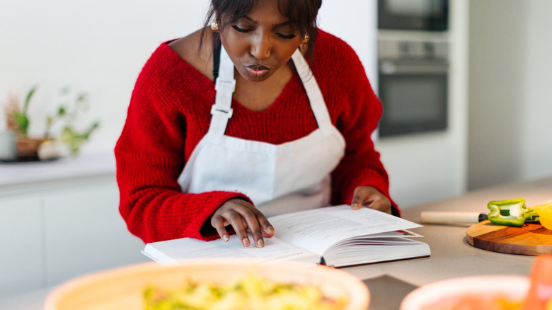 Woman reading recipe book while preparing food in kitchen