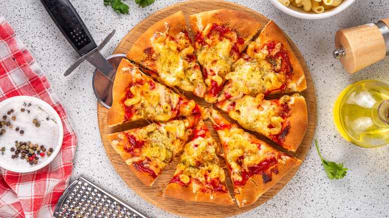 Sliced pizza on wooden serving board, topped with mac and cheese