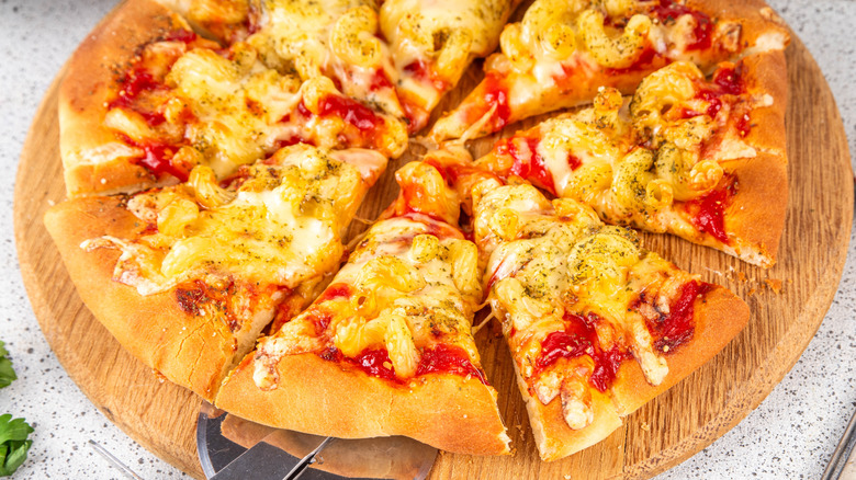 Sliced pizza on wooden serving board, topped with mac and cheese