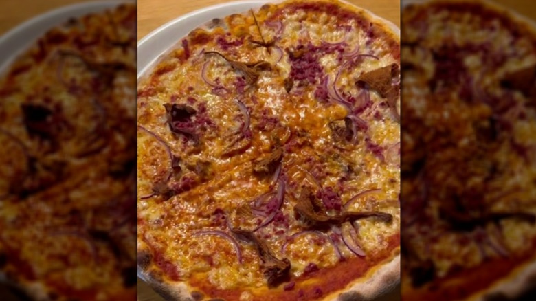 Close up of pizza Berlusconi with smoked reindeer and sliced red onions