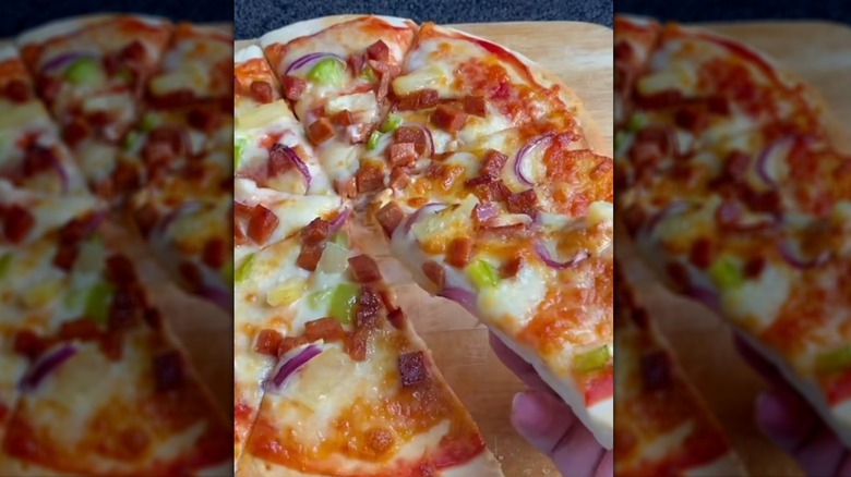 Hand lifting slice of pizza topped with cubed Spam and vegetables