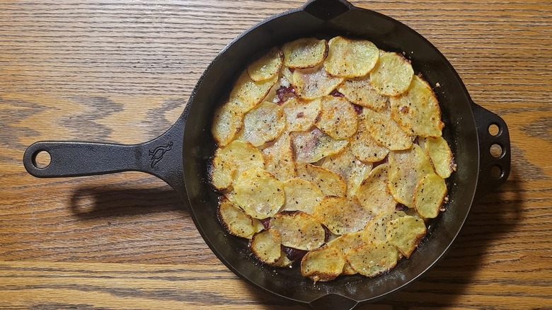 A cast iron skillet with pommes anna on a wooden table