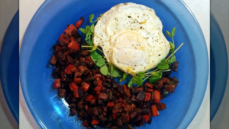 A blue plate of red flannel hash, served with an egg