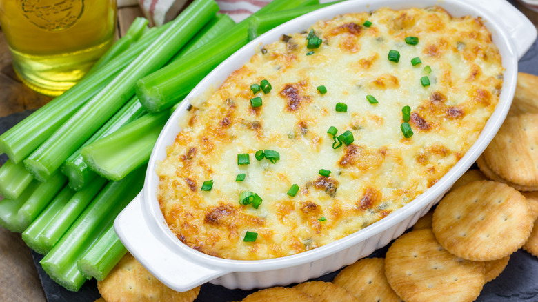 Hot crab dip in baking dish next to crackers and celery sticks