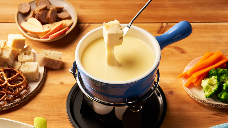 Dunking bread cube into pot of cheese fondue, surrounded by other dippers