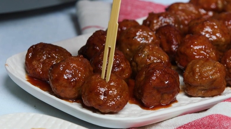 Grape jelly meatballs on plate, with one poked with wooden skewer