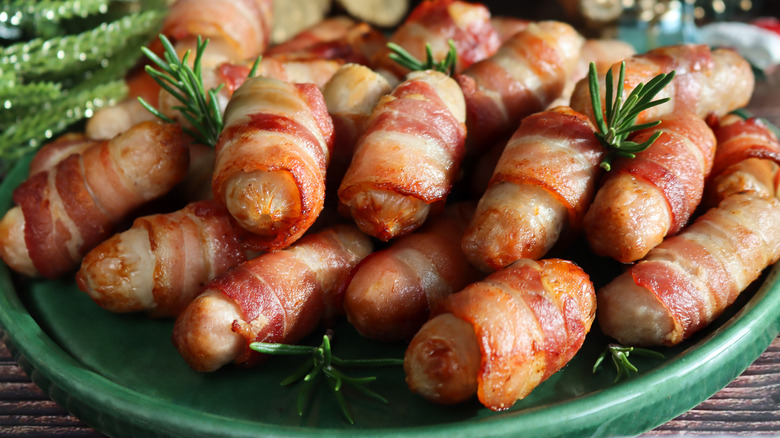 Pile of pigs in blankets on plate with sprigs of rosemary