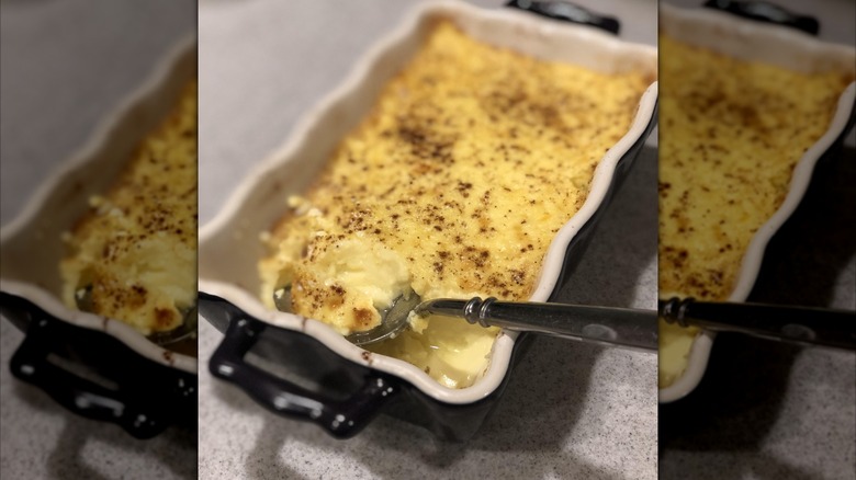 Mirrored image of baked custard in black casserole dish with spoon