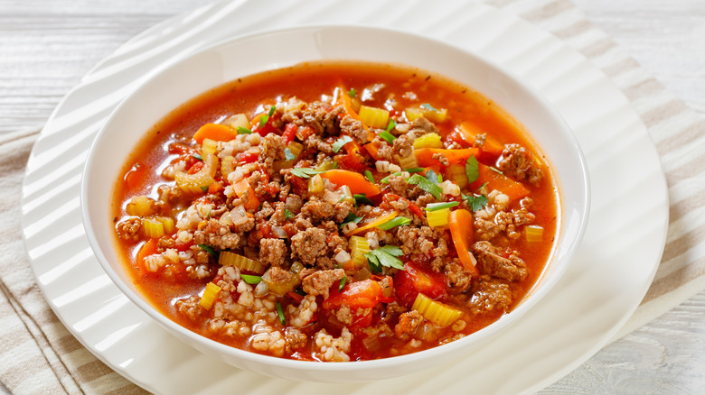 Hamburger Soup with barley and vegetables in white bowl on white wood table