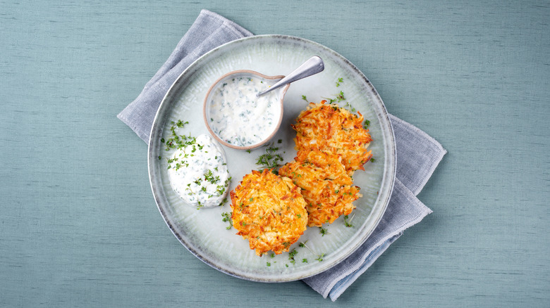parsnip cakes with chives and white dip on plate on blue background, photographed from above