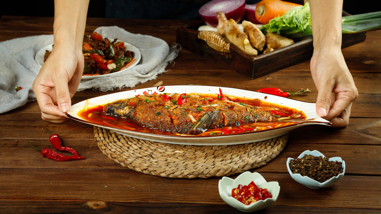 braised whole fish in spicy red sauce being set on a trivet