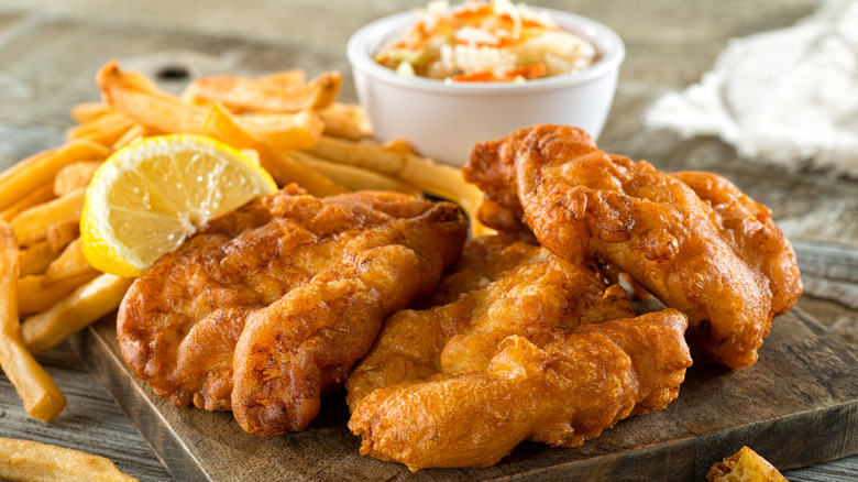 fish and chips shown on a wooden cutting board with small bowl of coleslaw