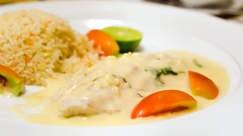 simple dish of fish fillet in creamy sauce, with a scoop of rice, tomato-wedge garnish and a half-lime