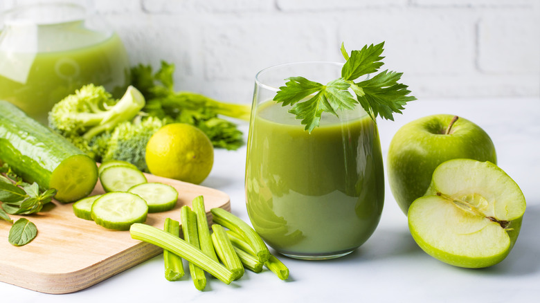 green smoothie in glass surrounded by green vegetables and Granny Smith apple