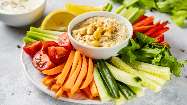 white plate full of sliced vegetables with a bowl of hummus in its center