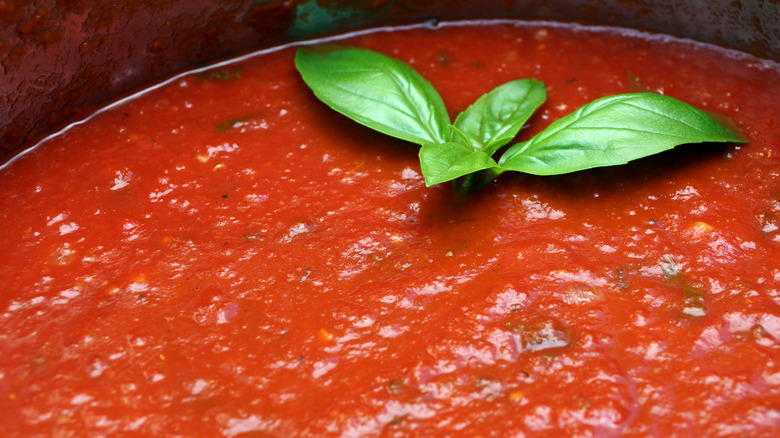 closeup of simmering marinara sauce with fresh basil leaves