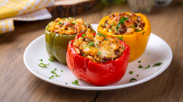 a white plate holding one each of a green, a red, and a yellow stuffed pepper