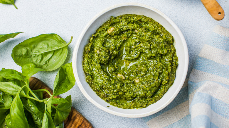 creamy pesto sauce on a blue table with basil on the side