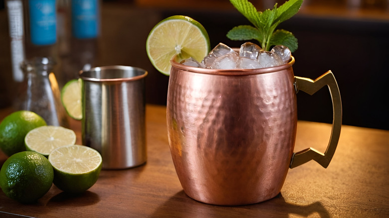 Ice-filled Moscow mule in a copper mug next to lime wedges