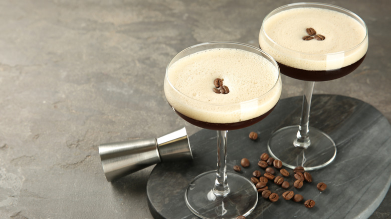 Two espresso martinis with thick foam next to coffee beans