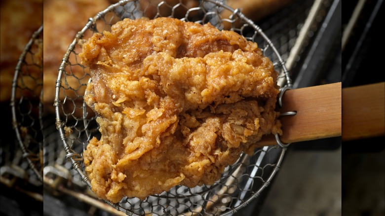 Fried chicken in a basket coming out of hot oil sitting on a wired strainer