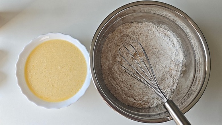 A bowl of flour with a whisk next to a smaller white bowl of wet batter
