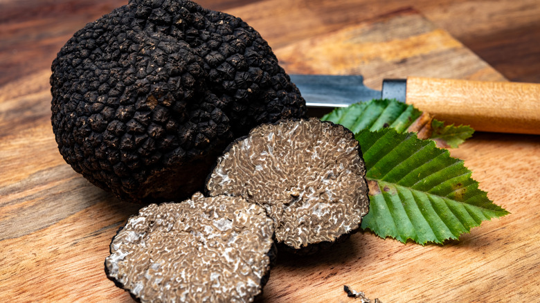 A whole black winter truffle with another truffle sliced in half and placed on a wooden board
