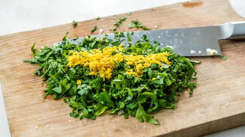 Gremolata ingredients like parsley and lemon zest on a wooden board