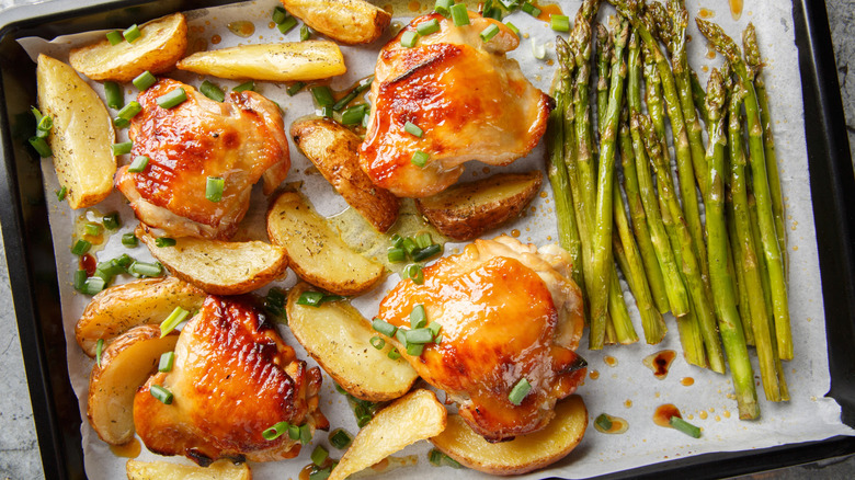 A sheet-pan of roasted chicken thighs, potato wedges and asparagus
