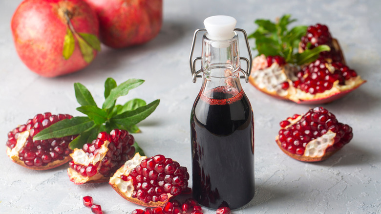 A bottle of pomegranate molasses next to some pieces of fresh pomegranate