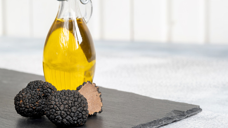 A carrafe of oil next to some whole black truffles