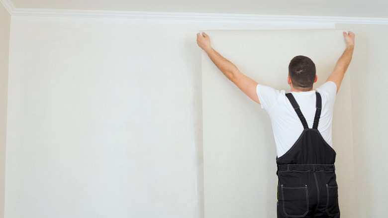 Man applying wallpaper on a white wall