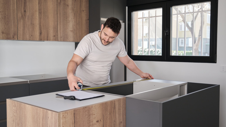 Man using measuring tape to install countertops in kitchen