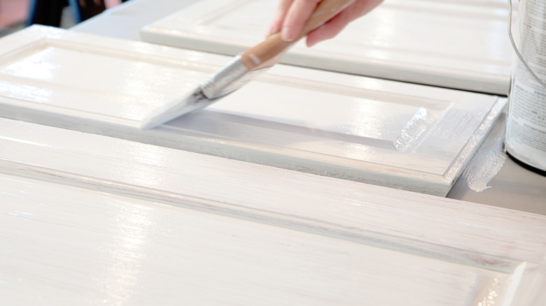 Close-up of hand painting a kitchen cabinet door white