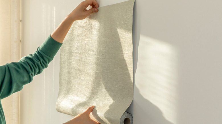 A pair of hands applying adhesive wallpaper to a well-lit wall