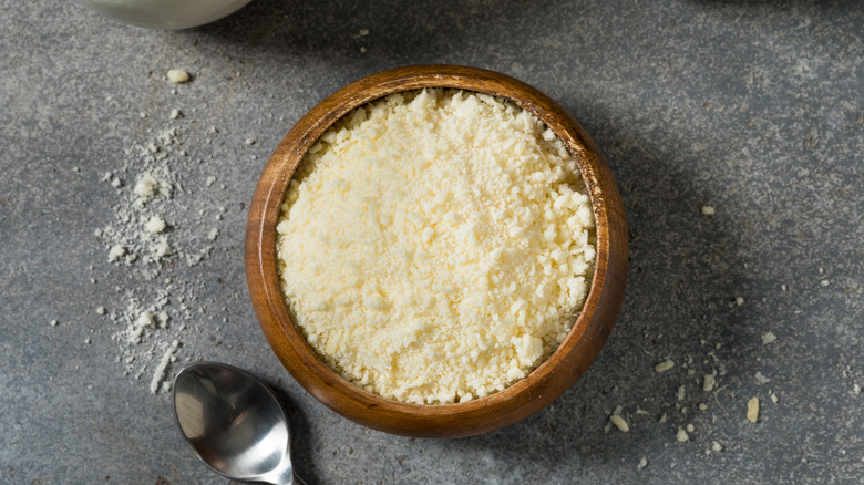 Grated Parmesan cheese in small wooden bowl next to spoon