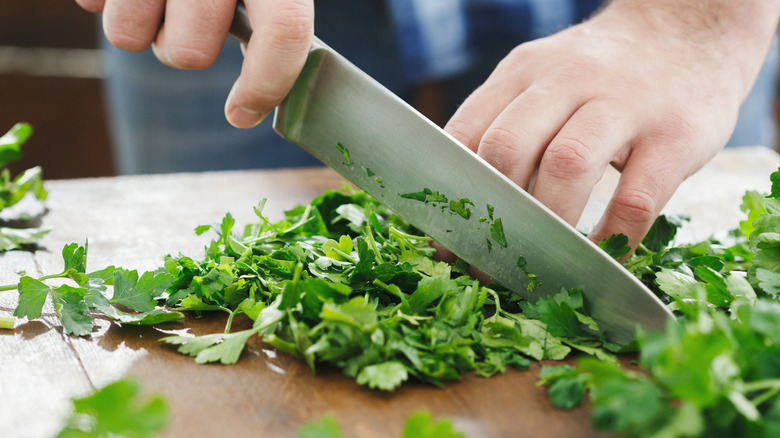 Knife chopping bunch of fresh parsley on wooden cutting board