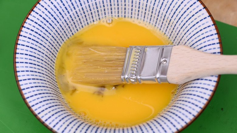 Bowl of beaten egg with pastry brush resting in it