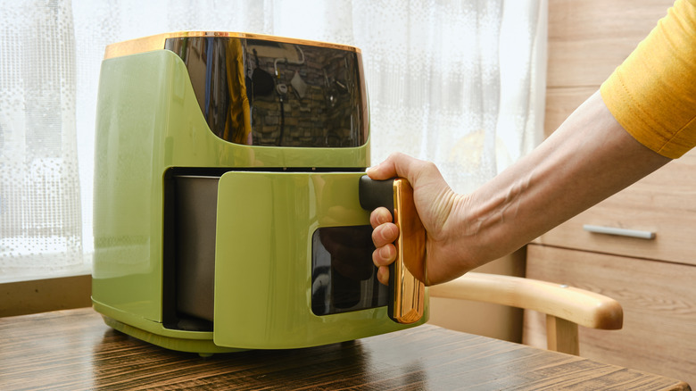 Hand opening basket of green and gold air fryer