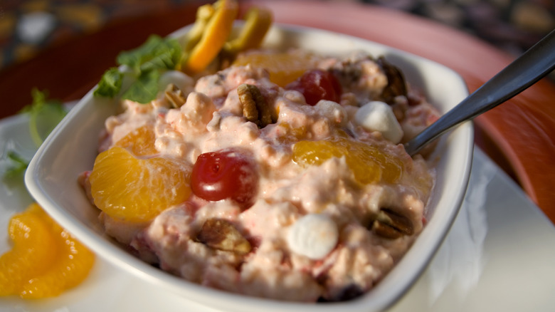 Bowl of Jell-O salad with mandarin segments, mini marshmallows, pecans, and maraschino cherries