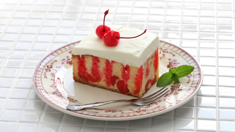 Slice of Jell-O poke cake topped with Cool Whip and maraschino cherries