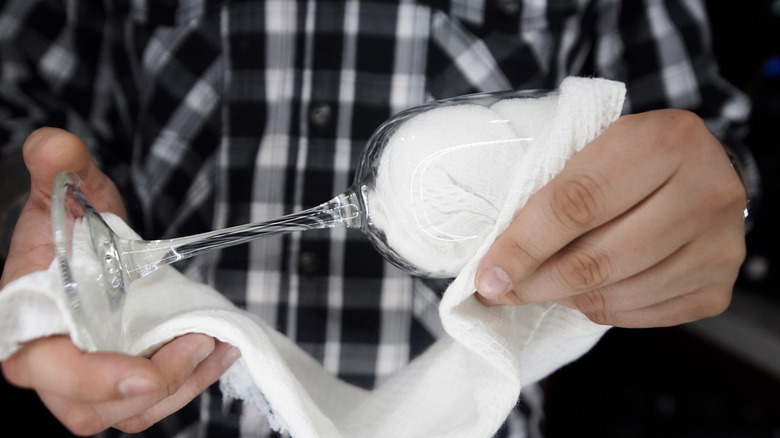 Man in a chequered shirt cleaning a glass with a white cloth