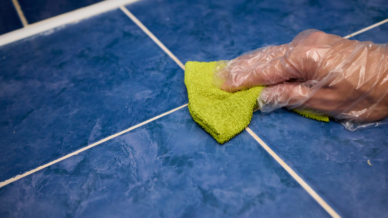 Blue tiles and grout being cleaned with a yellow cloth