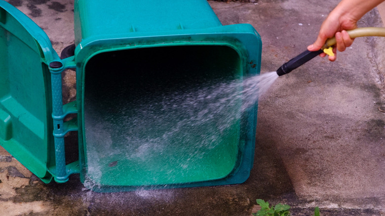 A hose spraying water to clean a green garbage can
