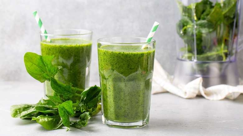 Two glasses of green juice with paper straws and fresh green leaves used as a decoration