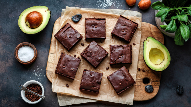 Avocado brownies on a wooden tray with avocado halves and chocolate chips on the side