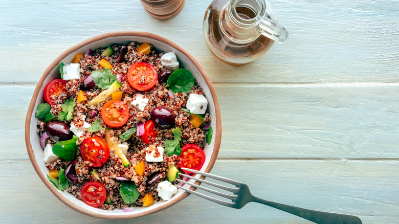 Quinoa, tomato, and feta salad in a bowl with a fork and dressing on the side