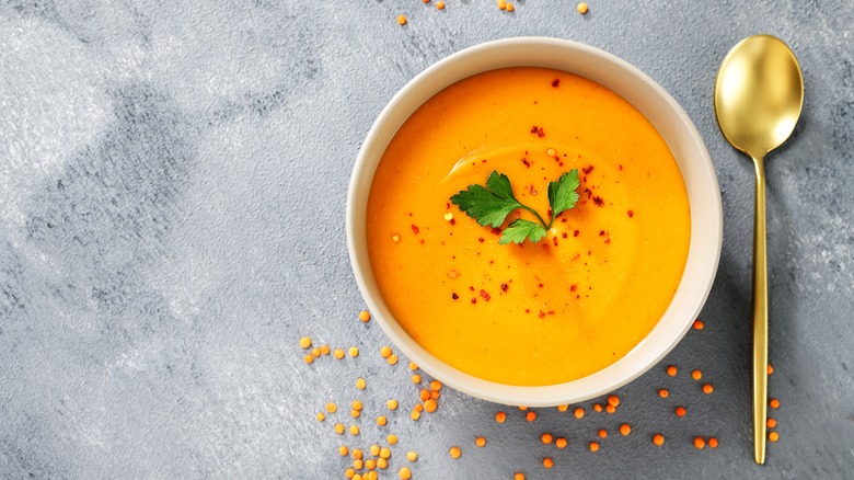 Red lentil soup in a white bowl with a spoon on the side